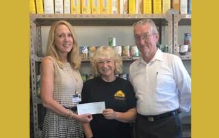 Smiling group holding a check while standing in food pantry.