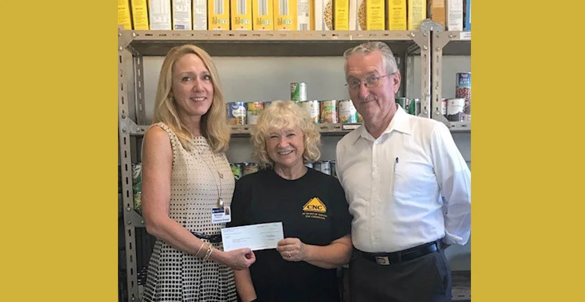 Smiling group holding a check while standing in food pantry.
