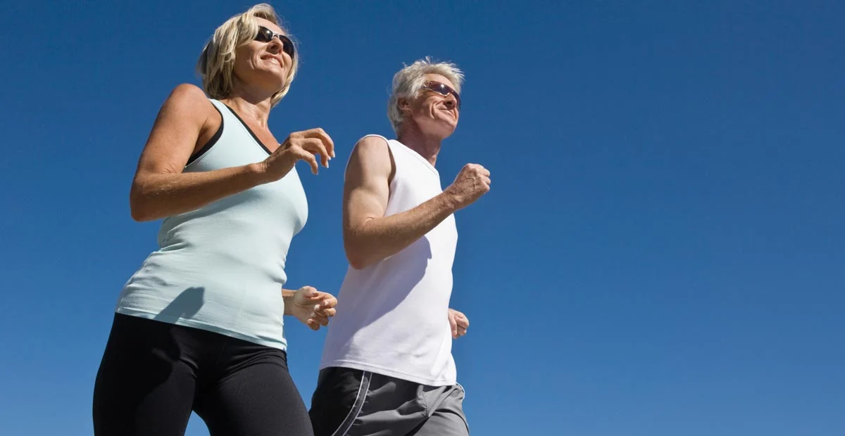 Mature couple running together outdoors with a clear blue sky behind them.