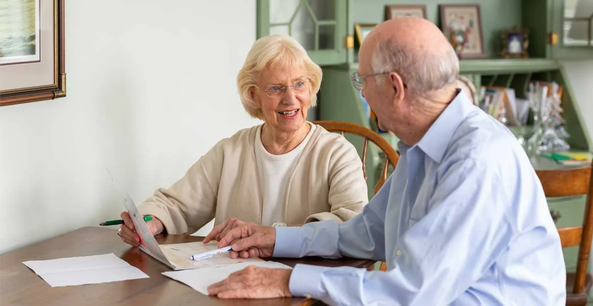 Smiling senior couple discussing paperwork at their kitchen table.