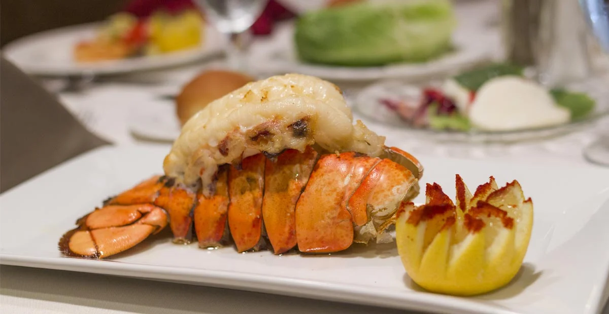 Cooked Lobster Tail on a white plate with seared lemon.