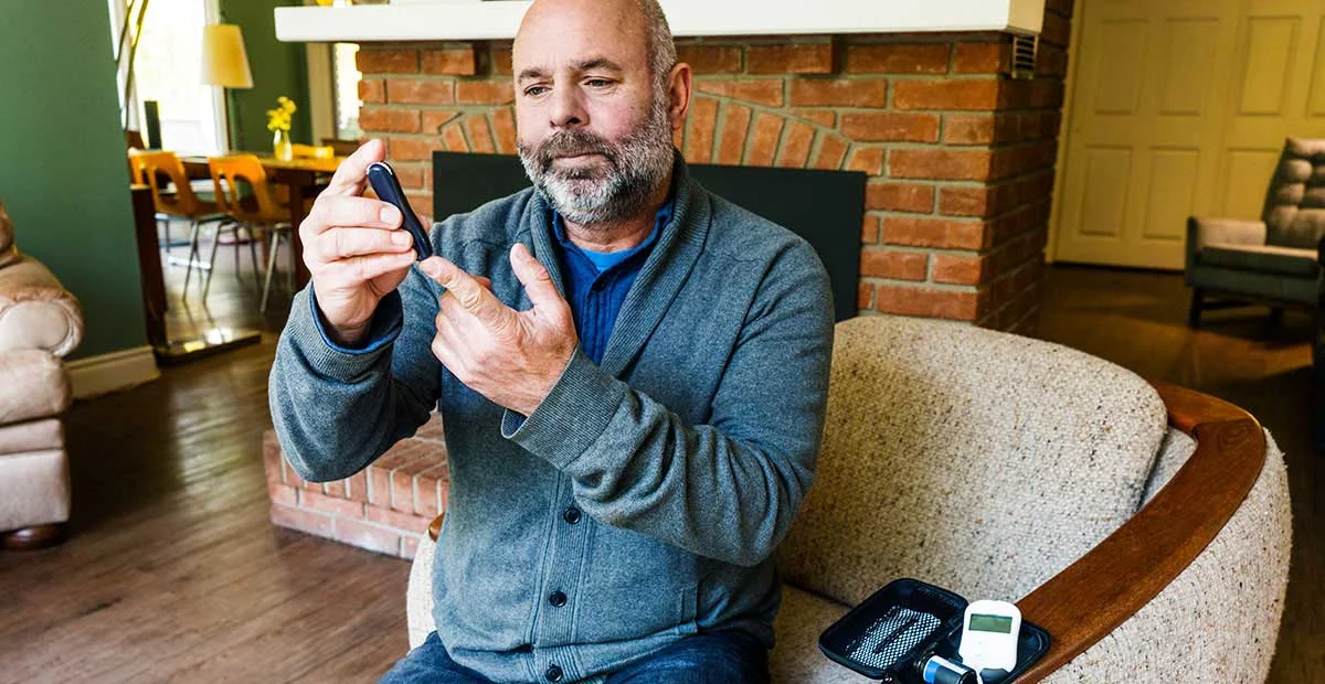 Man Testing Blood Glucose at home while seated in a chair.
