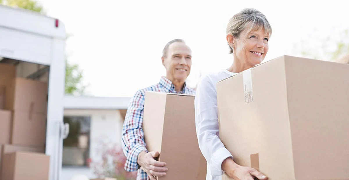 Couple carrying moving boxes outdoors away from a moving truck.