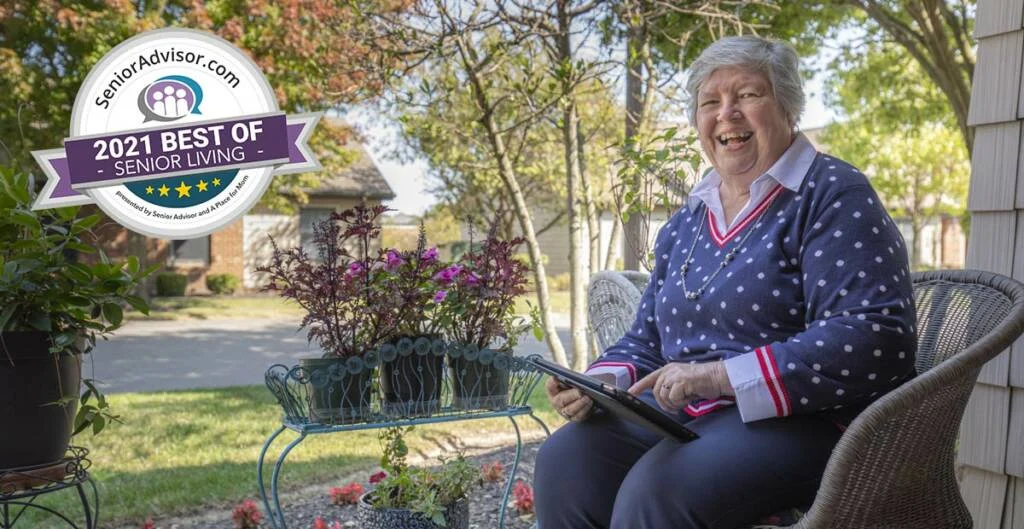 Smiling senior woman using a tablet while seated in a chair on her porch. There is a "2021 Best of Senior Living" badge overlaying the image.