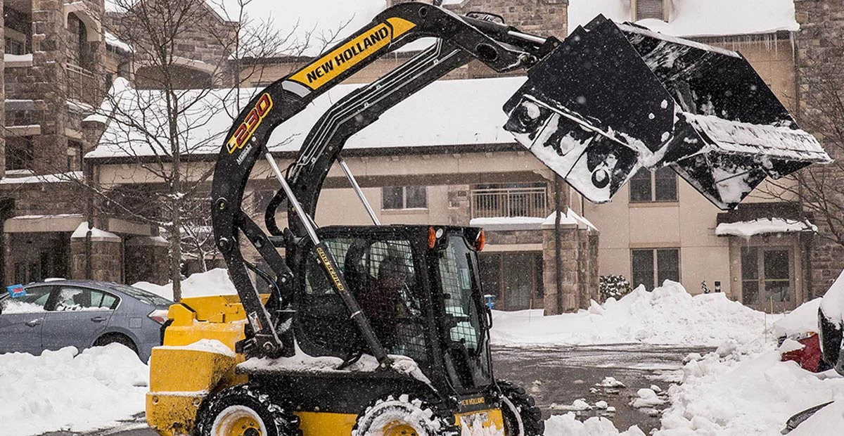 Plowing equipment working to clear a parking lot in a snowstorm.