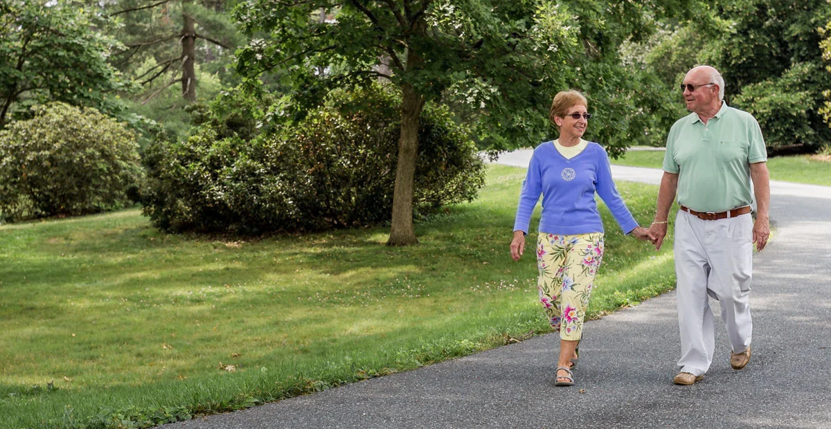 Senior couple walking on wooded path while holding hands.