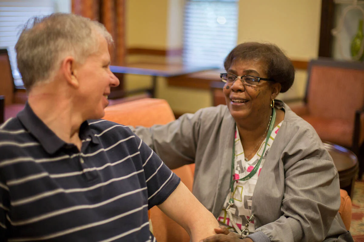 Smiling nurse talking with seated senior man.