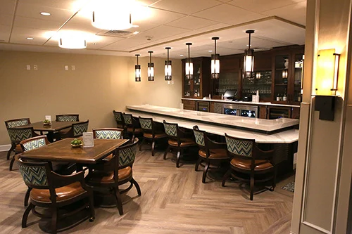 Pub Cozy pub with a well-stocked bar behind a marble counter. Chairs are pulled up to counter. Tables set with chairs are scattered in the pub.