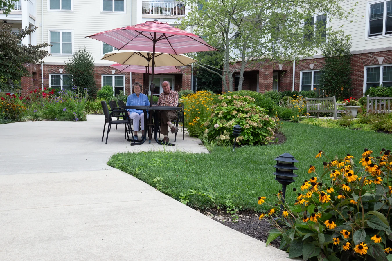 Smiling senior couple sitting at a picnic table surrounded by flowers.