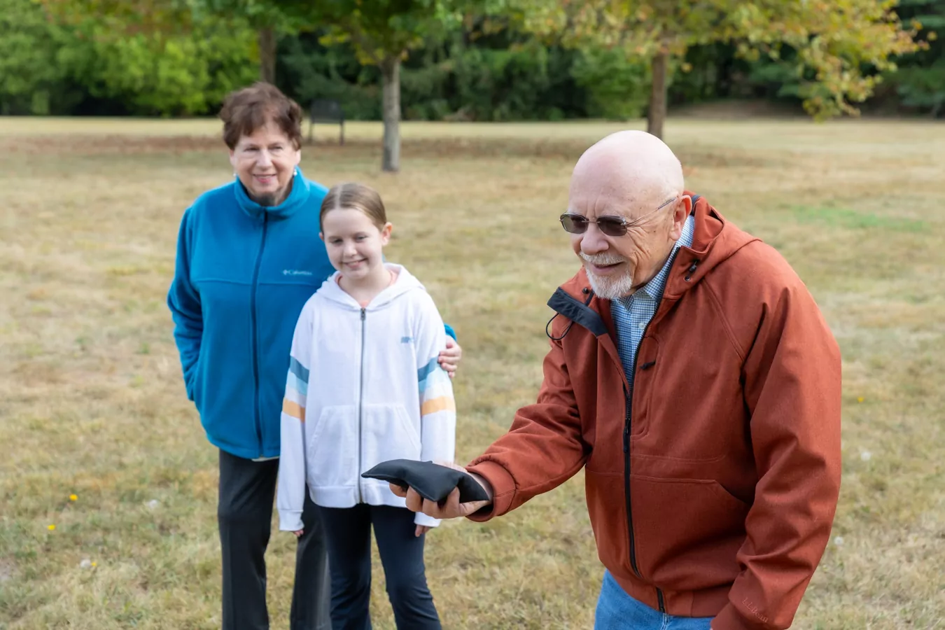 Man getting ready to throw bean bag in game of cornhole with woman and grandchild in the background