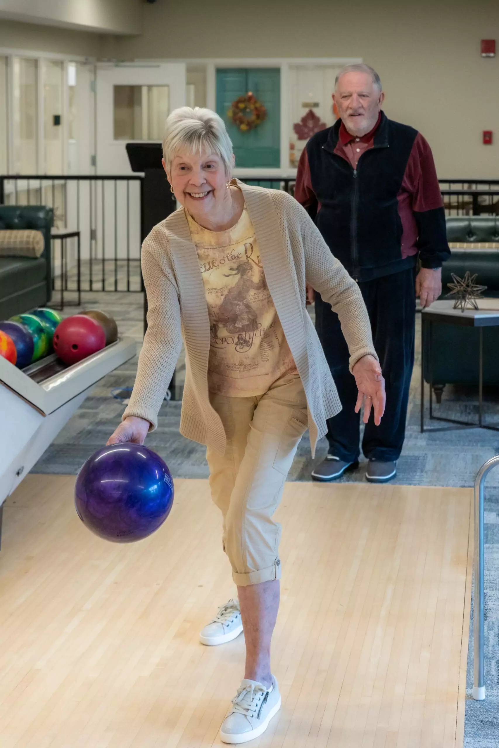 Smiling woman bowling with man in the background