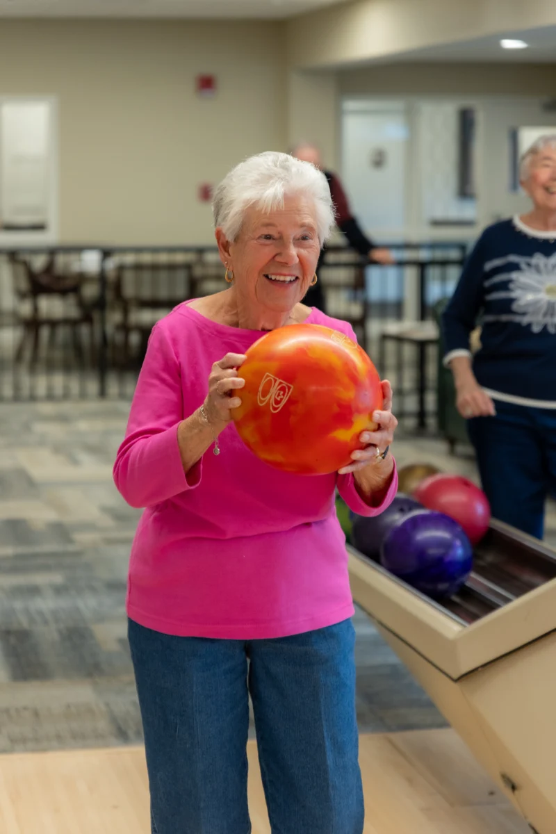 Senior woman bowling. Smiling senior woman holding bowling ball while standing in an indoor bowling alley.