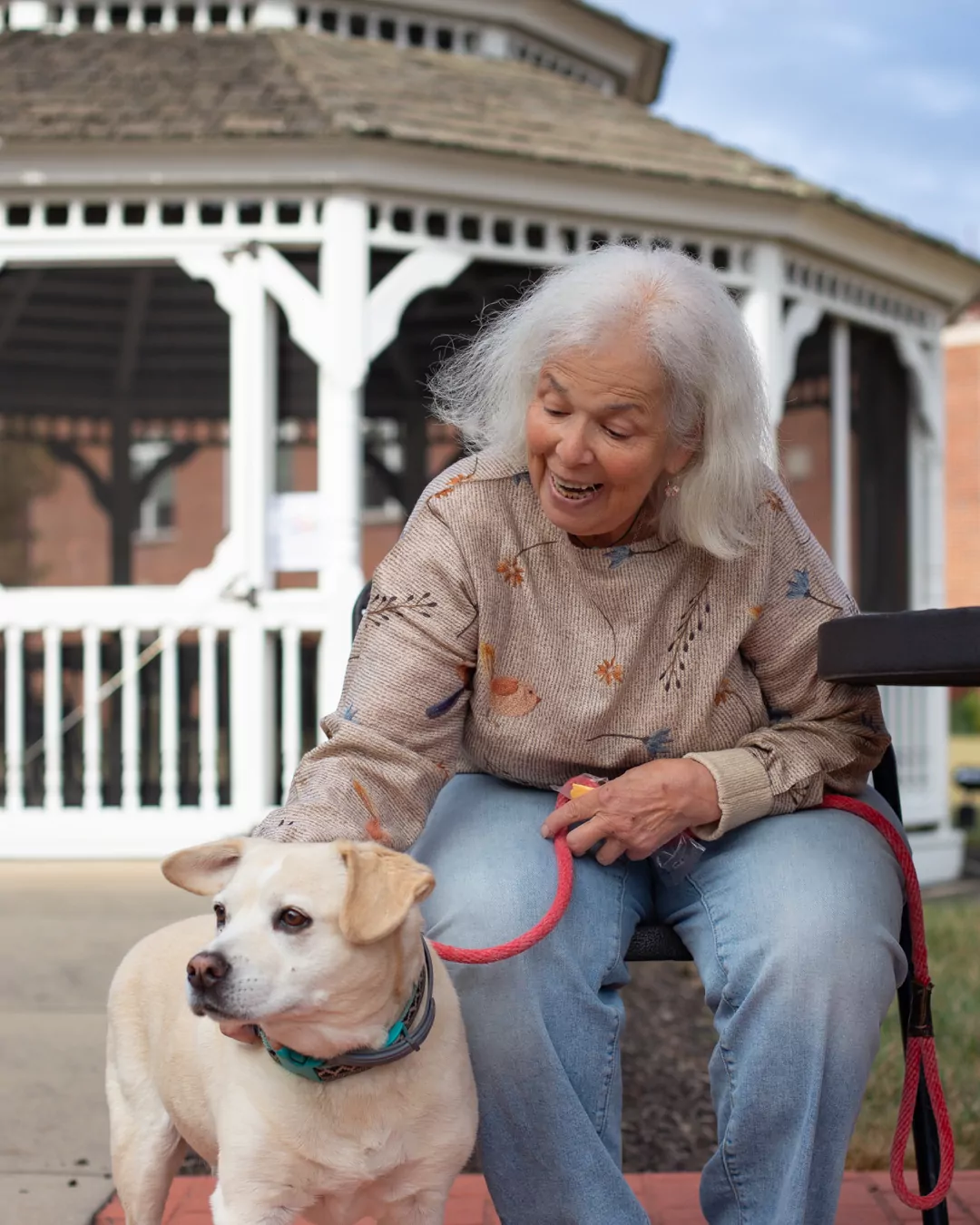 Woman leaning down to pet her dog while sitting at picnic table outside
