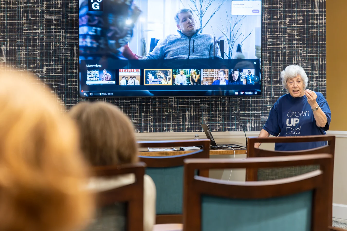 Senior woman speaking to others with documentary behind her.