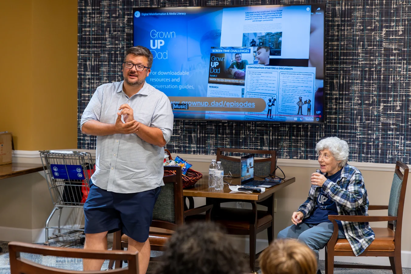 Man standing at front of room with his mother speaking to residents