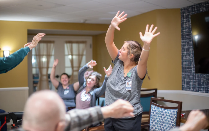 Three women at front of a room showing varied exercises to senior audience.