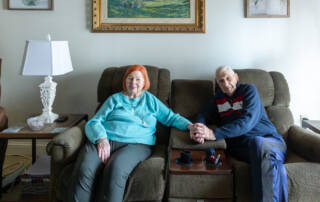 Smiling couple seated on their couch, holding hands.