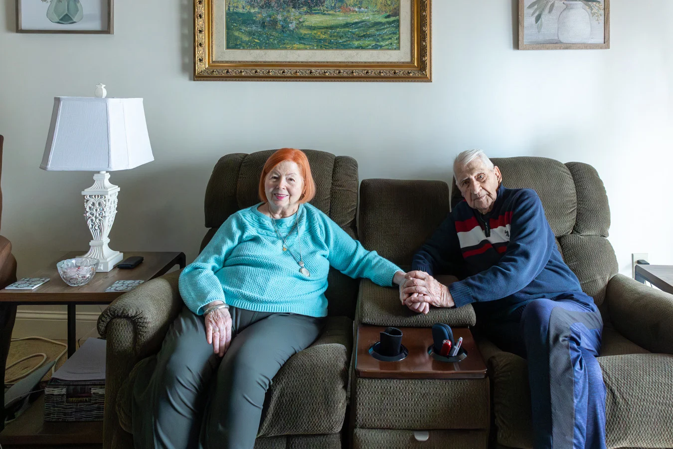 Smiling couple seated on their couch, holding hands.