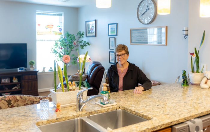Smiling senior woman sitting at her kitchen countertop.
