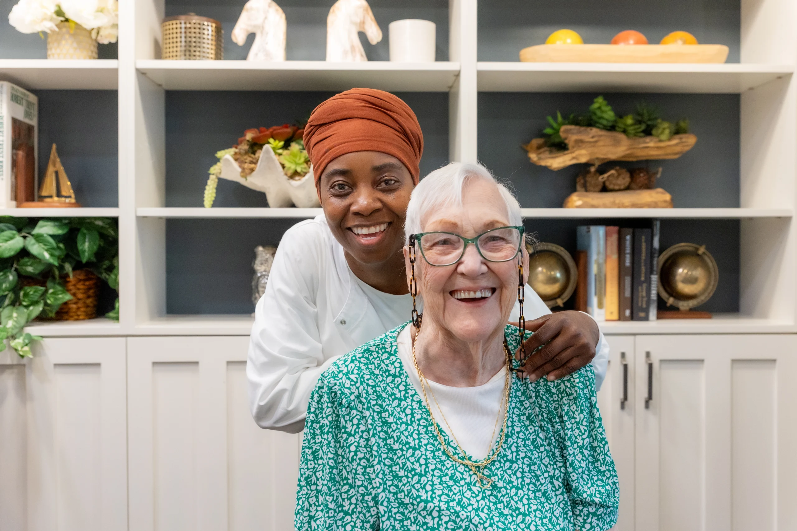 Smiling senior woman posed with a smiling nurse standing behind her.