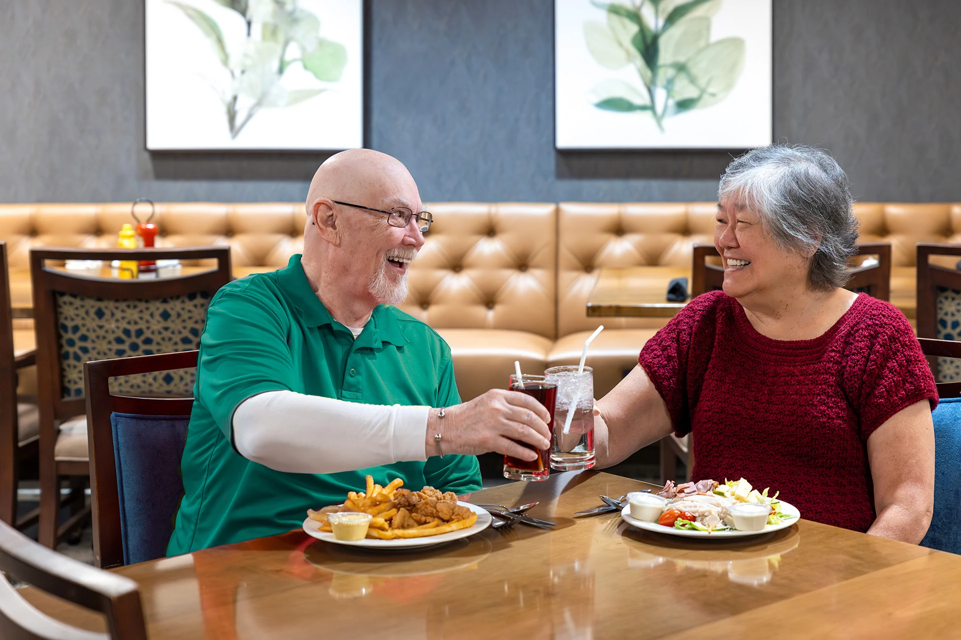 Smiling couple raising their glasses while eating lunch together in a cozy bistro.