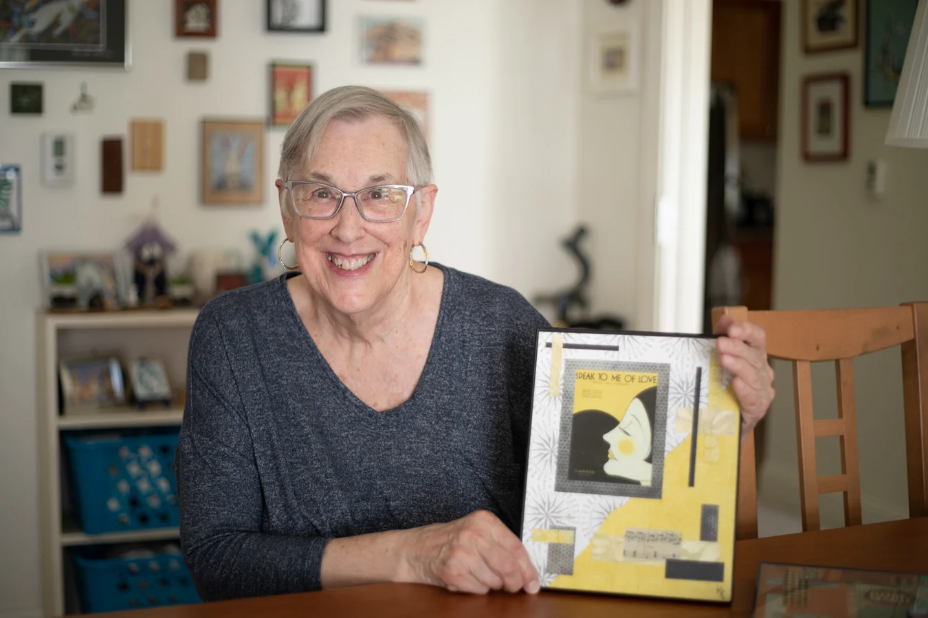 DU3A3587 Smiling senior woman seated at a table while holding up a book.