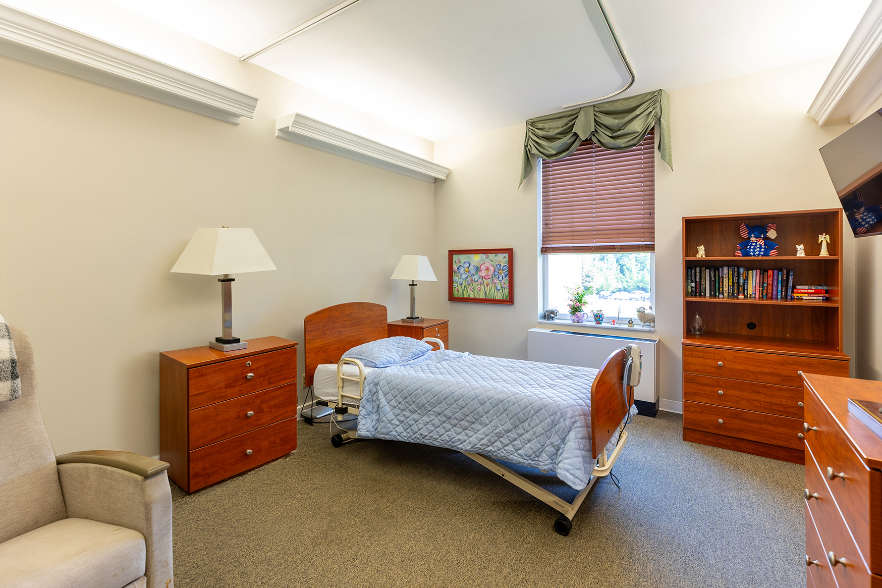 Nursing Room MVLH Brightly lit room with a bed, bookshelf, and night stand.
