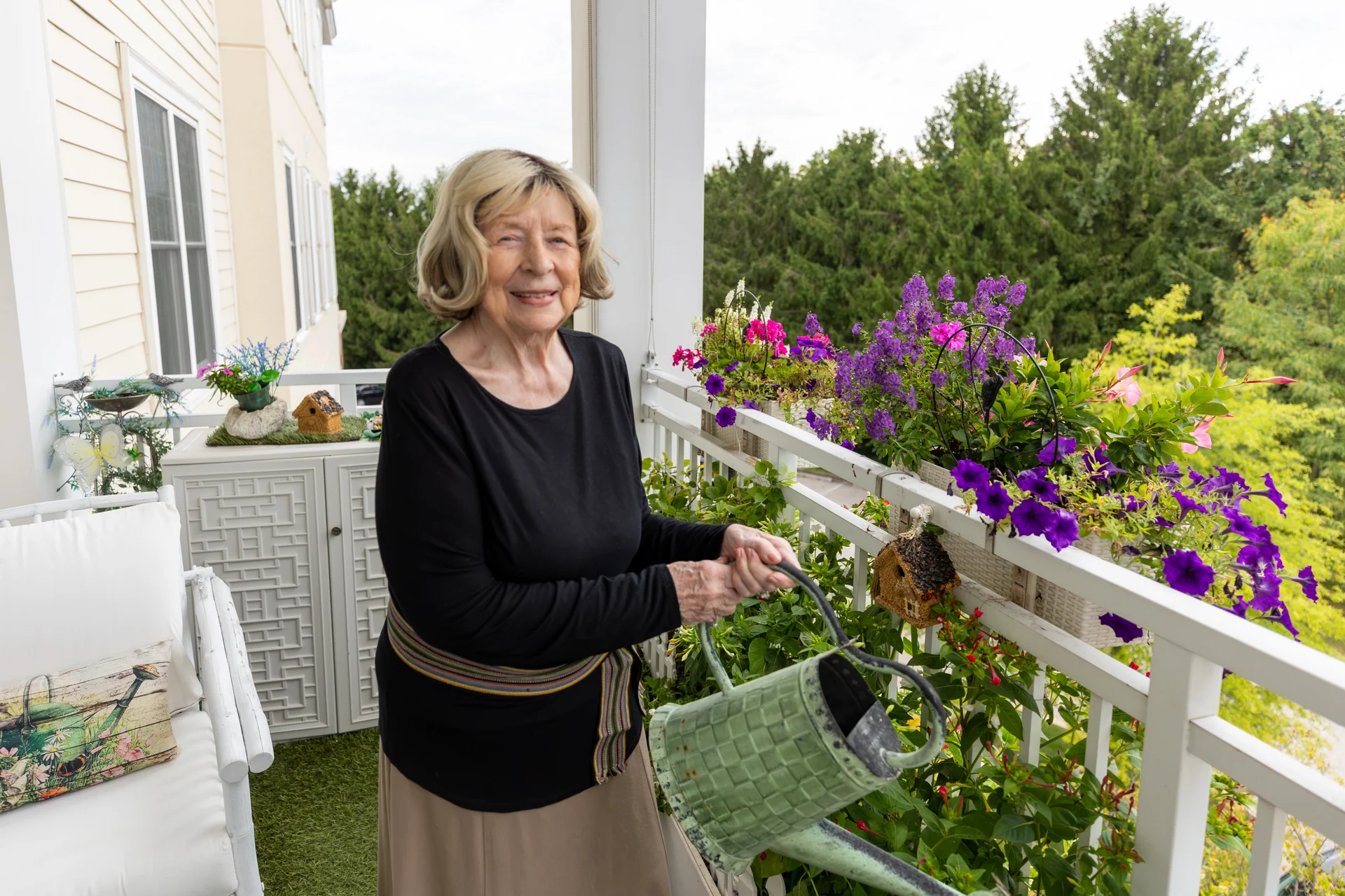 Smiling senior woman watering flowers on her porch outdoors.