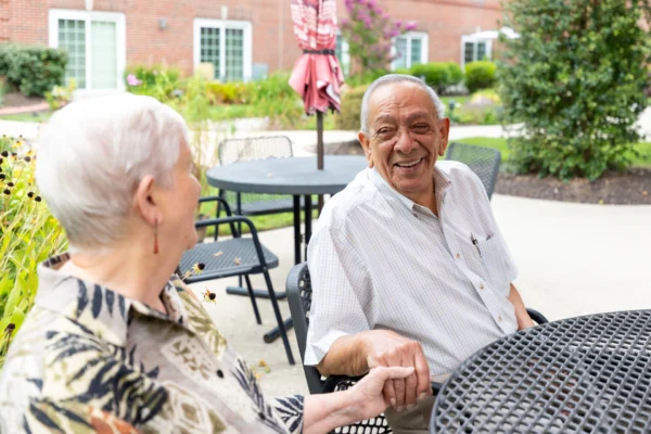 Smiling senior couple holding hands while seated at a picnic table.